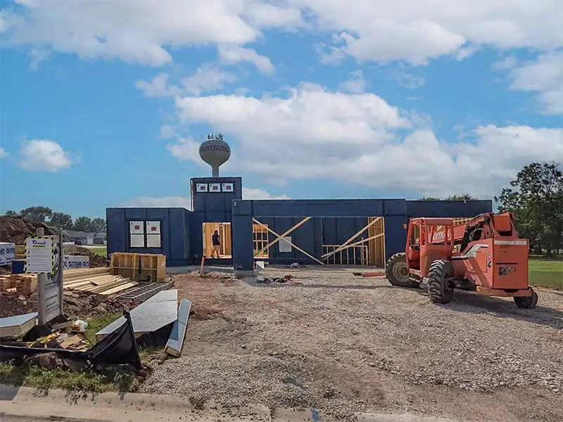 Commercial framing project with a water tower in the back, framing tools and machinery in to the right and left of the building.