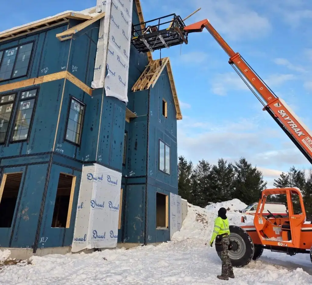 Newly framed two story house. Framing worker on a lift on the right hand side of the building.